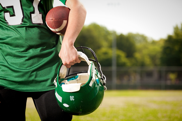 football player standing on field with helmet in hand
