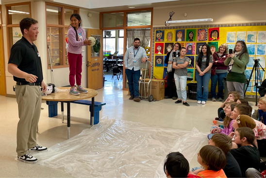 St. Charles Athletic Trainer guides a third grade student through a melon drop demonstration at a Train Your Brain event.