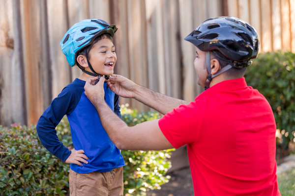 dad securing helmet on son