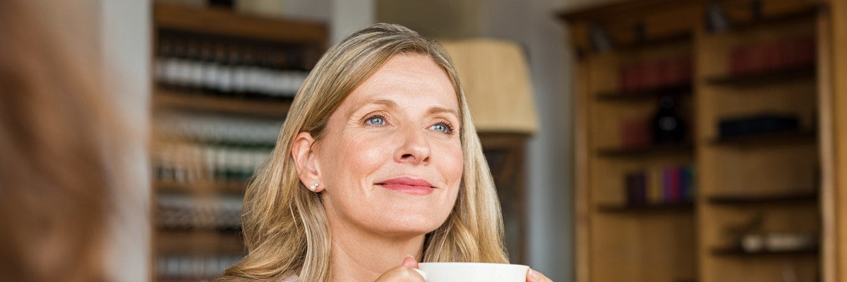 blonde woman looking into distance with cup of coffee in hand