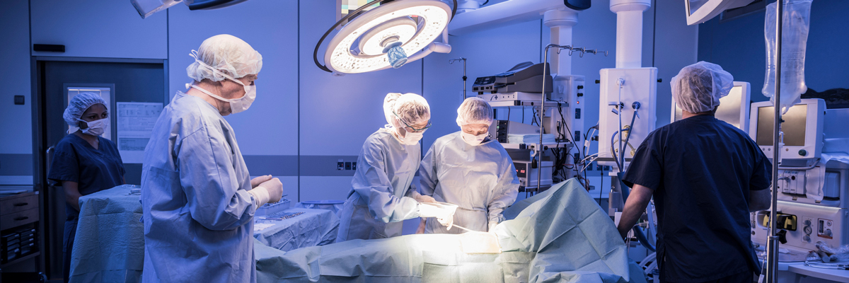 an operating room with health care professionals standing around table.